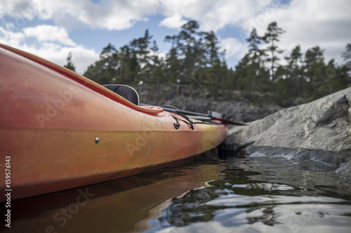 Kayak stands moored on a stony seashore, in the background of a cliff, forest and sky.