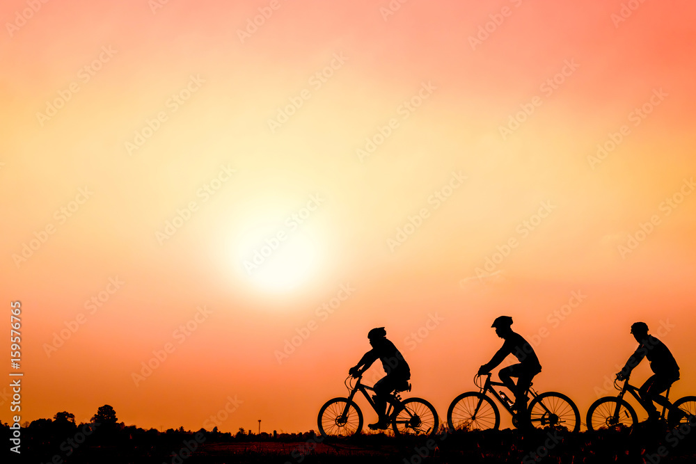 Obraz premium Silhouette of cyclists riding bikes on road at sunset.