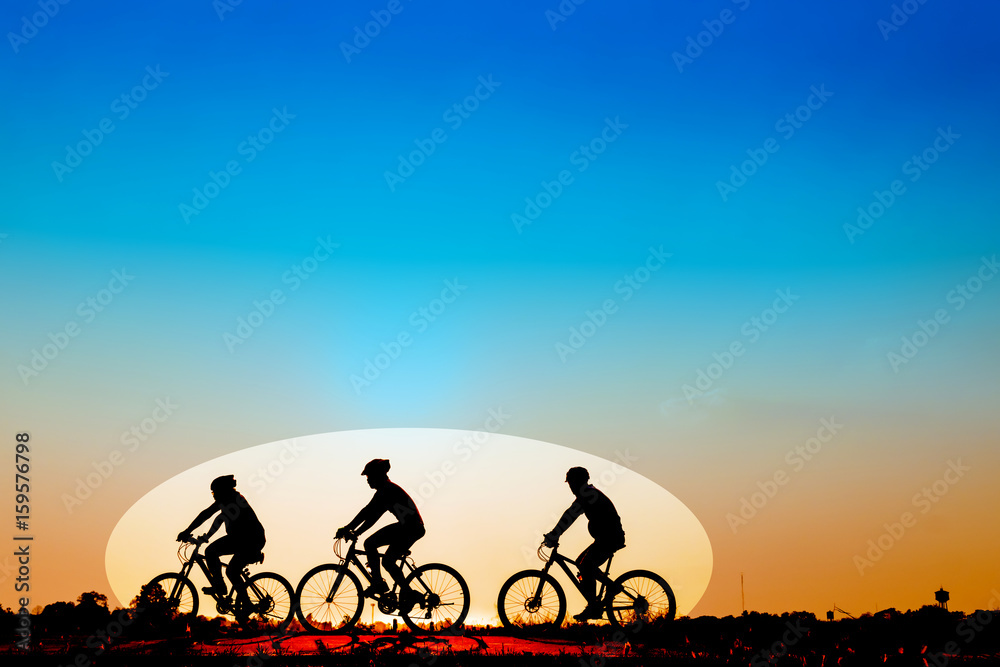 Obraz premium Silhouette of cyclists riding bikes on road at sunset.