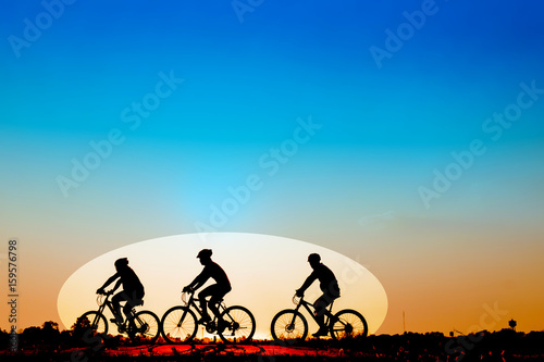 Silhouette of cyclists riding bikes on road at sunset.