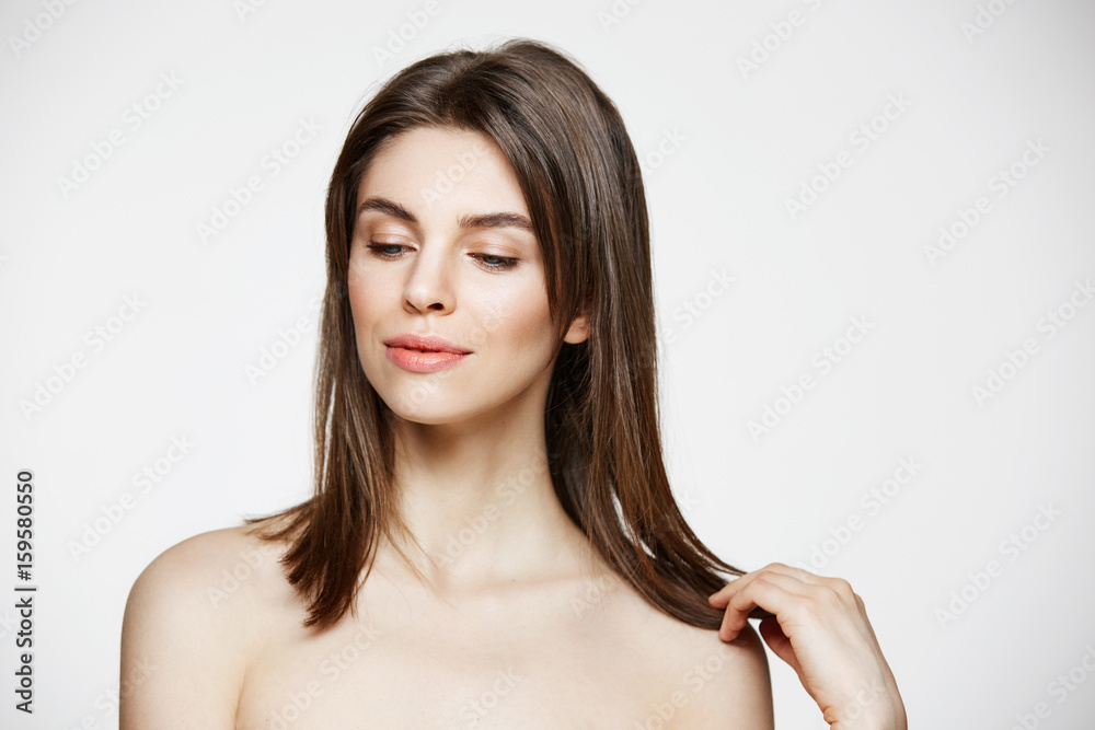 Fototapeta premium Portrait of young brunette beautiful girl smiling touching hair over white background. Spa beauty healthy and cosmetology concept.