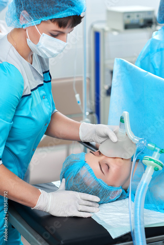 Vertical shot of a nurse working in operating room holding oxygen mask on a female patient during surgery medicine healthcare profession occupation concept.
