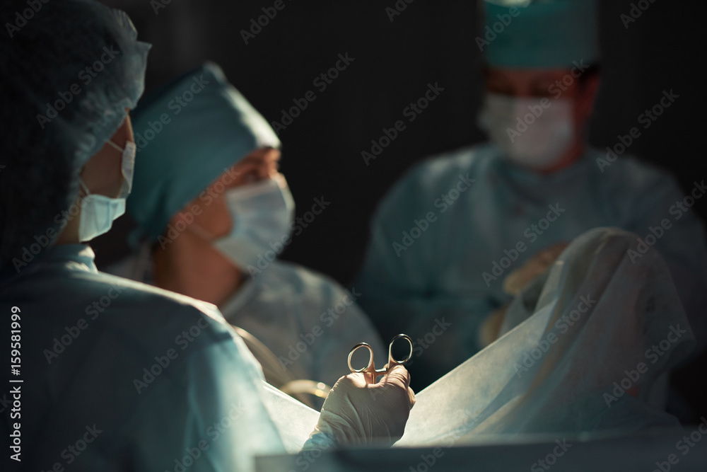 Rearview shot of a nurse assisting team of surgeons during surgery in operating room profession occupation job teamwork colleagues concept. Rearview shot of a nurse assisting team of surgeons during surgery in operating room profession occupation job teamwork colleagues concept.