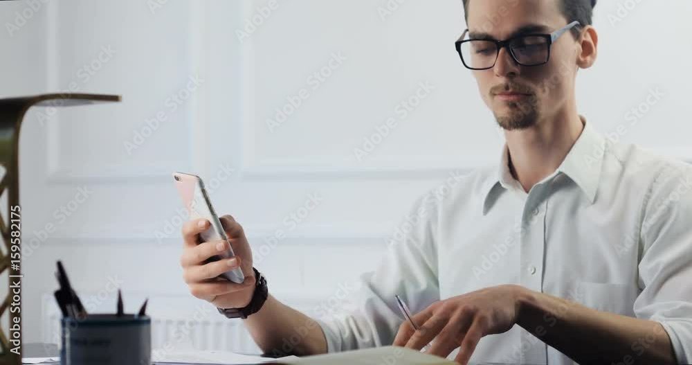 Attractive young business man working at office, looking on his smartphone, bright contemporary small creative business. Casual young man in new creative business office or architects company 4k Attractive young business man working at office, looking on his smartphone, bright contemporary small creative business. Casual young man in new creative business office or architects company 4k