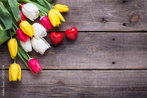 Little decorative hearts and bright spring tulips flowers on wooden background. Selective focus. Flat lay. Place for text..