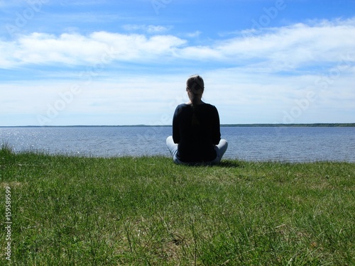Woman looks at the lake sitting on the beach