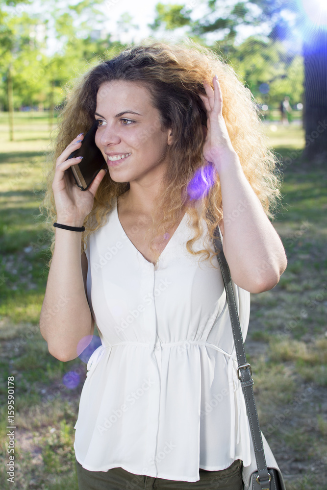 Girl calling on the phone and looking in the distance. Beautiful curly haired girl outdoors.