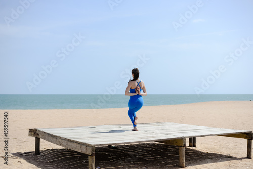 Morning training on the beach. Beautiful female doing workout on sunny blue sky outdoors background. Healthy lifestyle exercises. Back side view of perfect fit shape body