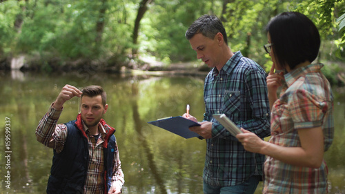 Three ecologists wearing casual clothing exploring lake and taking water sample. photo