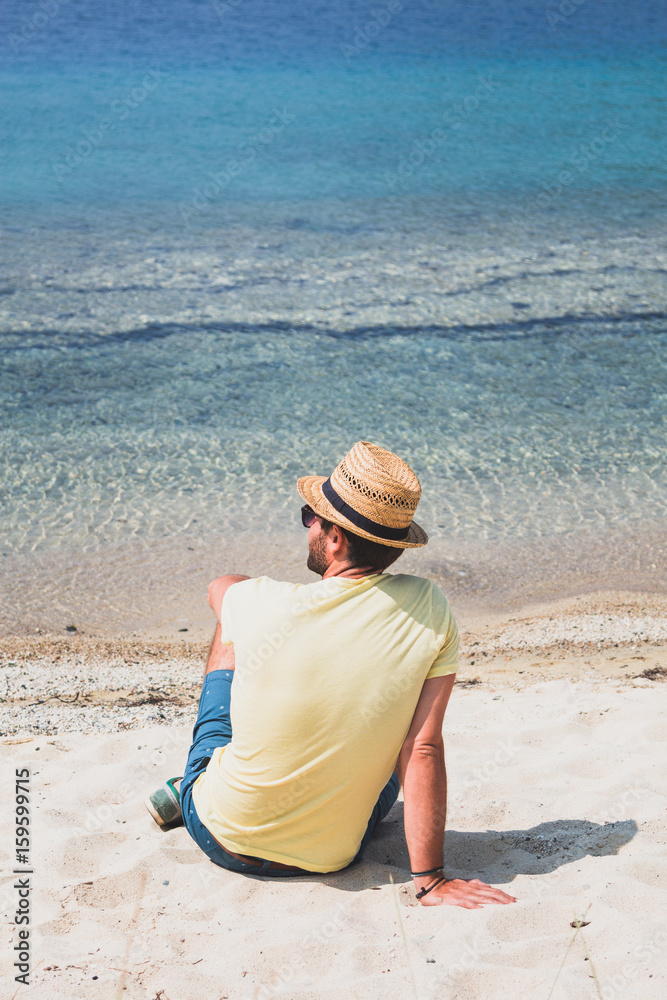 Young man sitting on the beach looking at sea