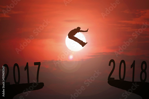 Silhouette of young man jumping between 2017 and 2018 years with beautiful sunset.