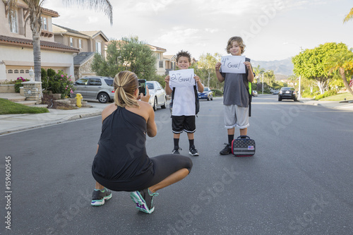 Mother photographing two schoolboy sons holding papers with handwritten school grade photo