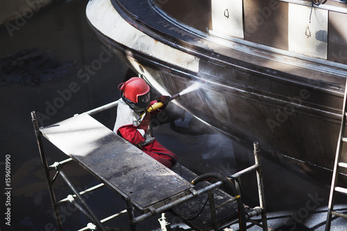 Worker cleaning hull of boat with high pressure hose in shipyard photo