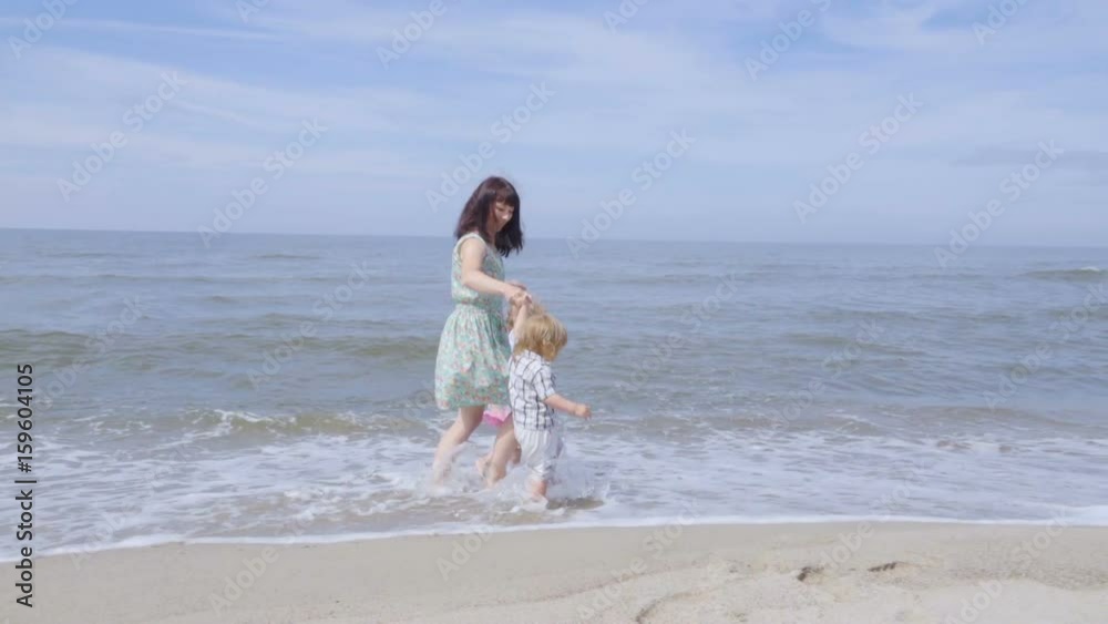 Happy family on the beach. Mother holds the arms of her son and daughter walking along the seashore. Slow motion. Happy family on the beach. Mother holds the arms of her son and daughter walking along the seashore. Slow motion.