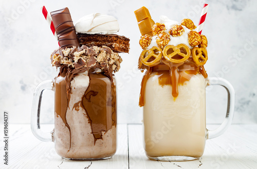 Caramel and chocolate indulgent extreme milkshakes with brezel waffles, popcorn, marshmallow, ice cream and whipped cream. Crazy freakshake food trend. photo