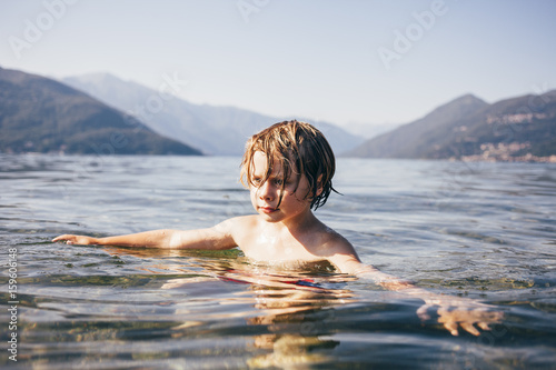 Mountain range and head and shoulders of boy in water arms open looking away, Luino, Lombardy, Italy