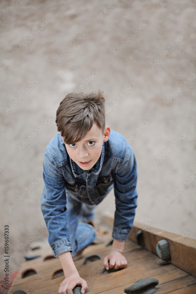 Teenager boy climbing a rope net outdoor on the kid playground. The climber trains simulator on the street. Teenager boy climbing a rope net outdoor on the kid playground. The climber trains simulator on the street.