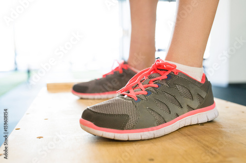 Feet of young woman in gym standing on wooden box.