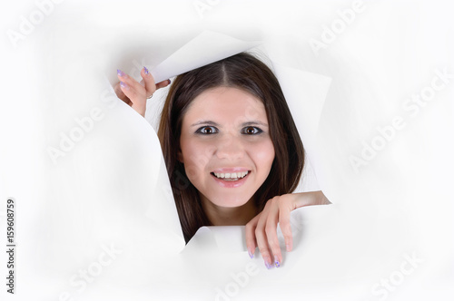 Cute young woman smiling looking and peeping through a hole in white paper