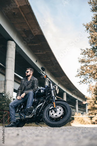 Man seat on the motorcycle on the city bridge. Handsome man with style and glasses. photo