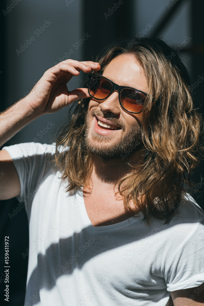 Close-up portrait of handsome smiling young man adjusting sunglasses and looking away Close-up portrait of handsome smiling young man adjusting sunglasses and looking away