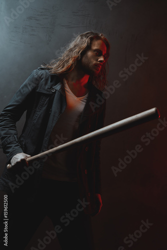 Young long haired man holding baseball bat ready to hit in darkness
