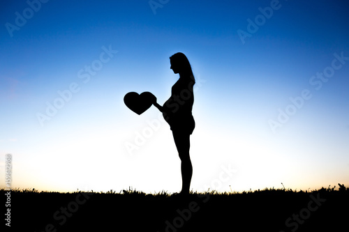 Pregnant woman touch her belly sit on the ground against the light