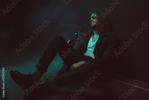 Tablou pe pânză young drunkard in sunglasses drinking whiskey from bottle while sitting on the f