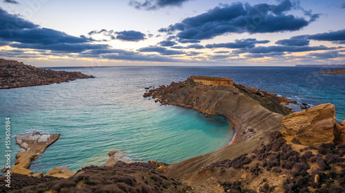 Mgarr, Malta - Panorama of Gnejna bay, the most beautiful beach in Malta at sunset with beautiful colorful sky and golden rocks taken from Ta Lippija