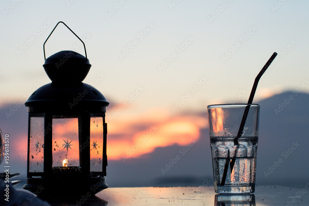 Lantern with burning candle glowing on the table with sea and sunset background