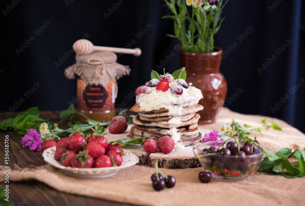 Delicious pancakes with berries and cream on the authentic wooden stand. Summer food still life concept.