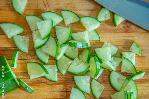 Small pieces of cucumber for salad on a wooden cutting board and cook knife