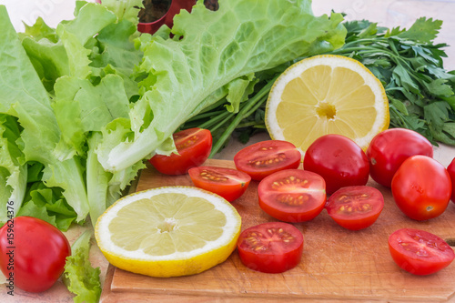 Cherry tomatoes  lemon plastics  parsley and lettuce leaves covered with drops of water lie on the kitchen table