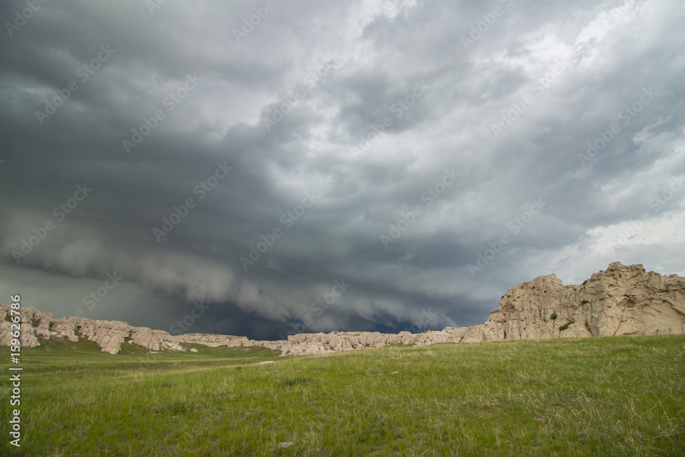 A low and ominous shelf cloud approaches rocky bluffs on a hillside in Nebraska.