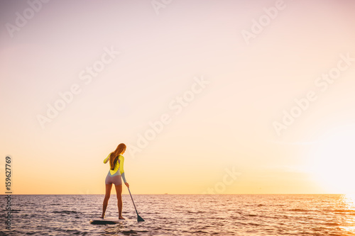 Slim sporty woman in ocean on stand up paddle surfboard with beautiful sunset colors © artifirsov