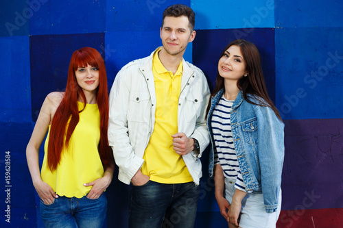 Three young stylish friends standing close on bright background