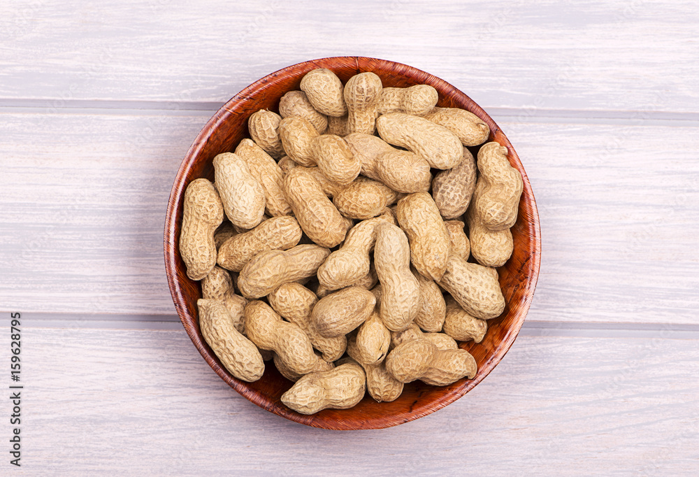 From above pile of whole peanuts in bowl on white wooden background. From above pile of whole peanuts in bowl on white wooden background.