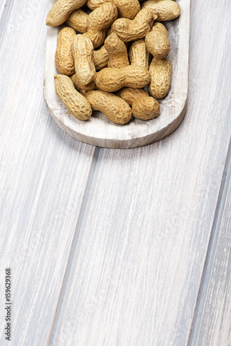 From above plate with whole peanuts on wooden bowl, on wooden table.  Copy space. Vertical studio shot.