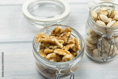 Walnuts and pistachios in glass containers on wooden table.