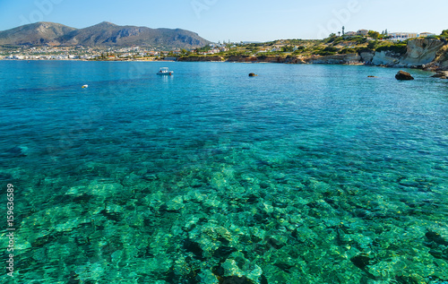 scenic views of the seabed with green stones, a city on the shore and a small boat in bay of island Crete, Greece.