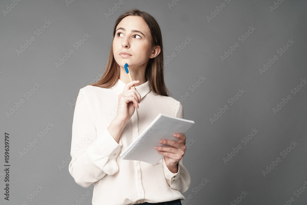 Portrait of businesswoman holding a notebook and pen in her hand. One is isolated on a gray background Portrait of businesswoman holding a notebook and pen in her hand. One is isolated on a gray background