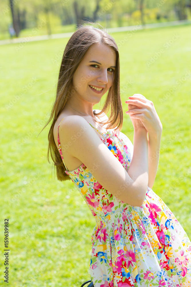 Obraz premium Portrait of young beautiful woman with long hair wearing flower dress in green spring park