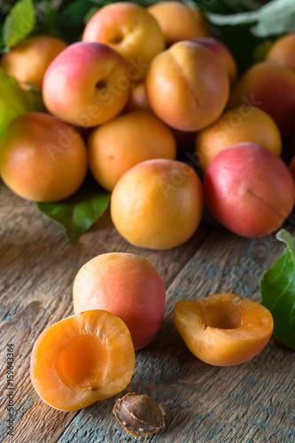Juicy fresh apricots with leaves on old wooden table .