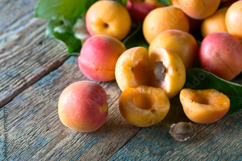 Juicy fresh apricots with leaves on old wooden table .