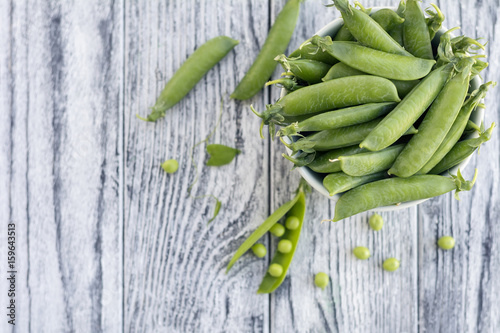 Green peas in white bowl on grey wooden background