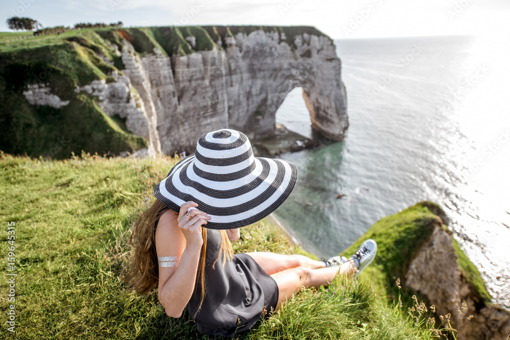 Young woman in striped hat enjoying great view on the famous rocky coastline near Etretat town in France