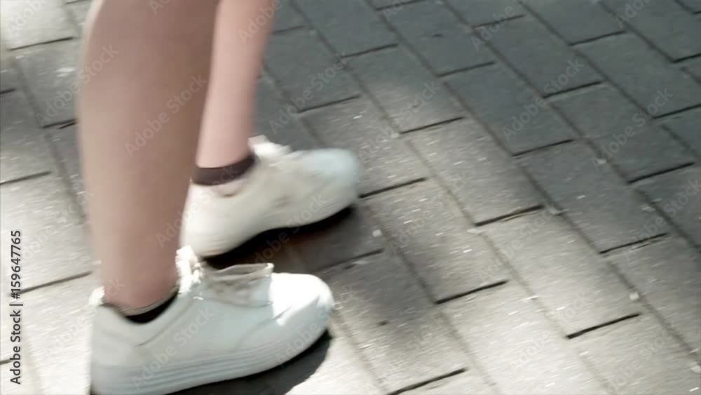 Woman in white sneakers walking forward alone. Steps on the asphalt. Woman in white sneakers walking forward alone. Steps on the asphalt.
