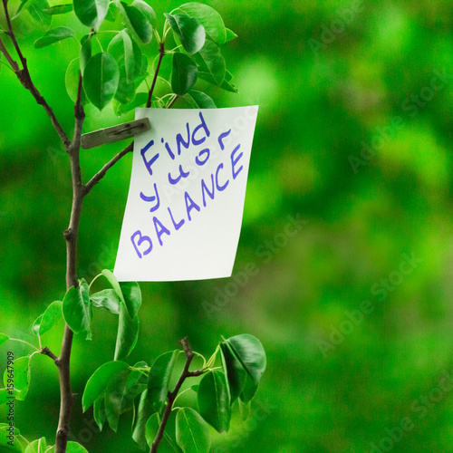 Motivating phrase find your balance. On a green background on a branch is a white paper with a motivating phrase