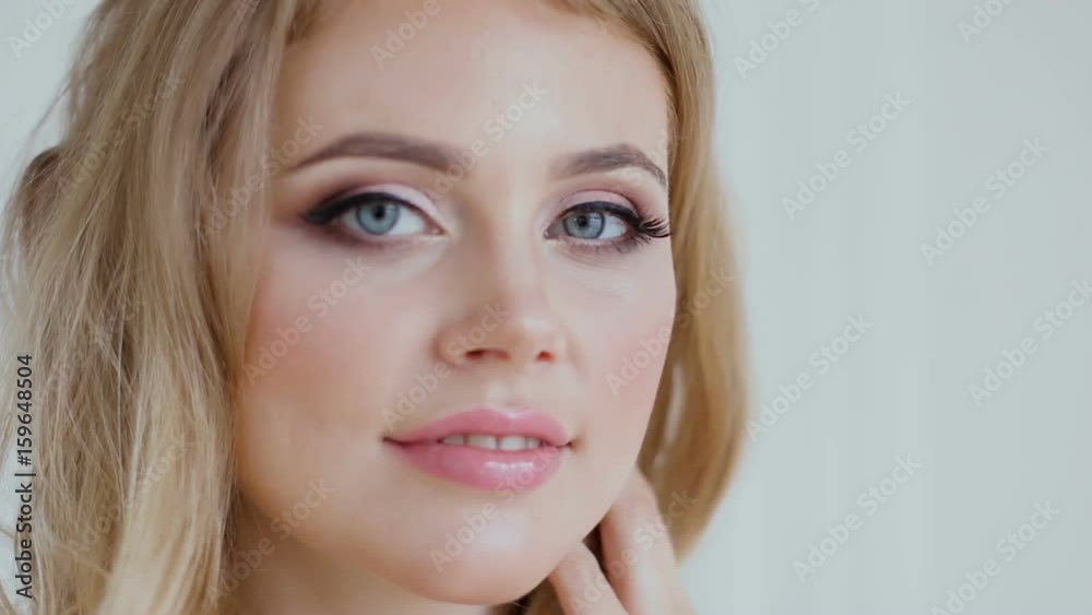 blonde girl adjusts her hair at home standing in a bright dress