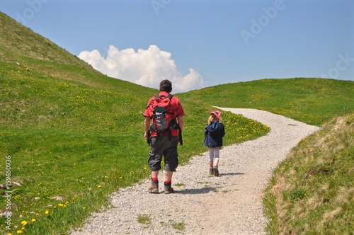 Vater mit Tochter am Wandern auf Wanderweg durch grüneWiesen und Hügellandschaft